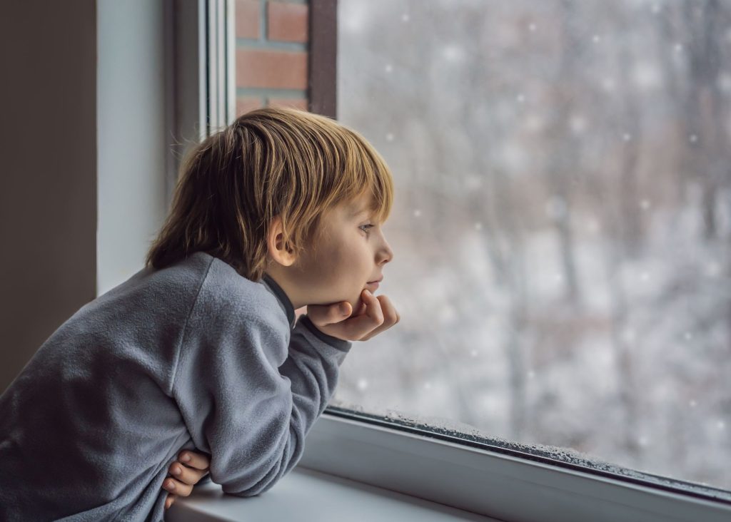 a photo of a child looking out the window as snowflakes fall