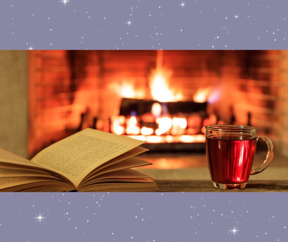 A photo of a fire in a fireplace with a glass of apple cider and a book in the foreground.